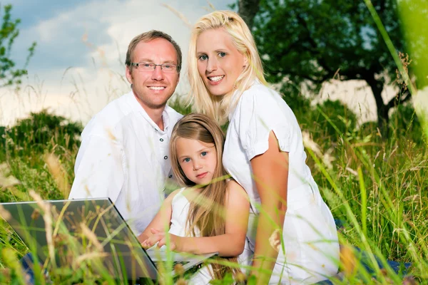 Familia feliz sentado en el prado con ordenador portátil —  Fotos de Stock