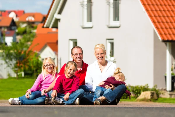 Happy family sitting in front of home — Stock Photo, Image