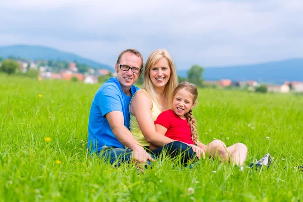 Glückliche Familie im Freien auf Gras sitzend — Stockfoto