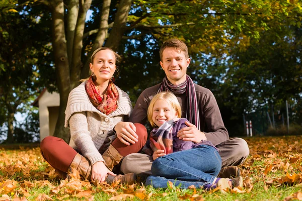 Šťastná rodina sedí venku na trávě na podzim — Stock fotografie