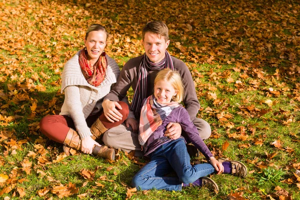 Glückliche Familie im Herbst im Freien auf Gras sitzend — Stockfoto