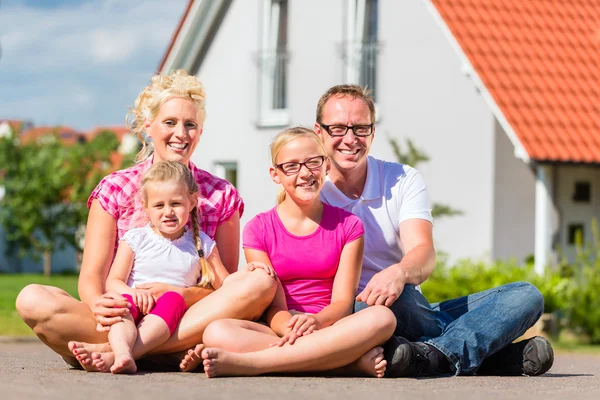 Family sitting on street in front of suburban house — Stock Photo, Image