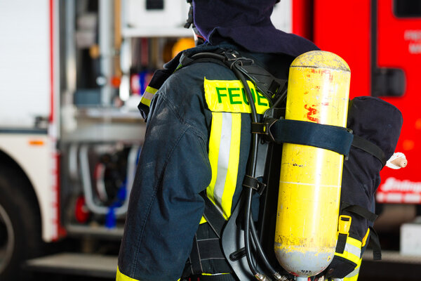 молодой пожарный в форме перед пожарной машиной
