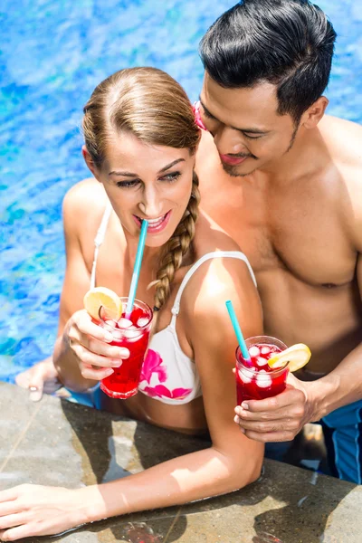 Couple in Asian hotel pool drinking cocktails