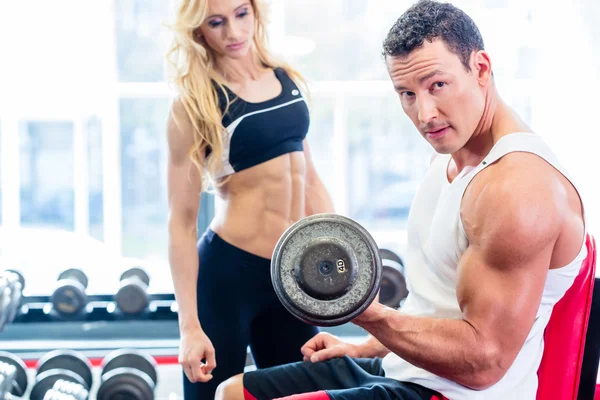 Couple in fitness gym with dumbbells lifting weight