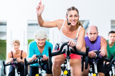 Senior people in gym spinning on fitness bike clipart