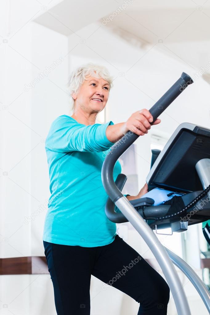 Senior woman on elliptical trainer exercising in gym