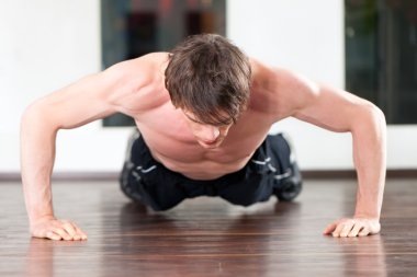 Adam spor salonunda şınav çekiyor.