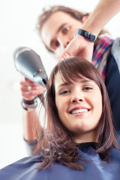 Перукар дує сухе волосся жінки в магазині — стокове фото