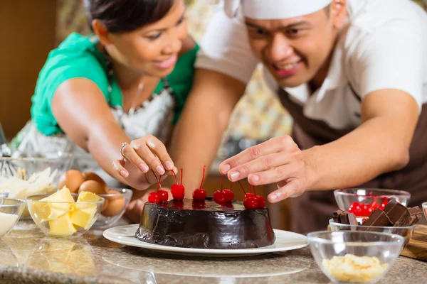 Asian couple baking chocolate cake in kitchen — Stockfoto