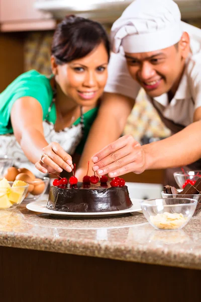 Asian couple baking chocolate cake in kitchen — Zdjęcie stockowe