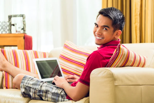 Pria Asia yang duduk di sofa berselancar di internet — Stok Foto