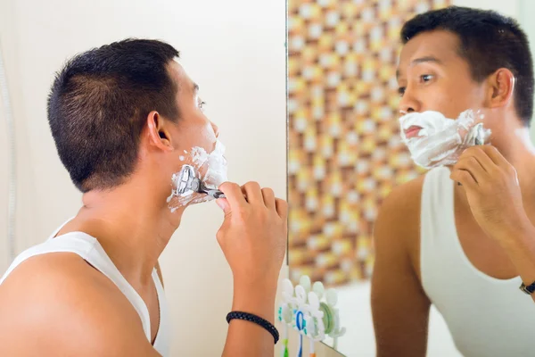 Asian man shaving in front of mirror — Stok fotoğraf