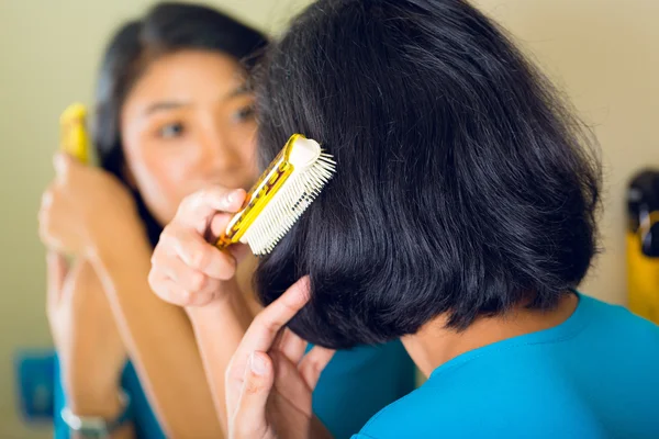 Asiatische Frau kämmt Haare im Badezimmerspiegel — Stockfoto