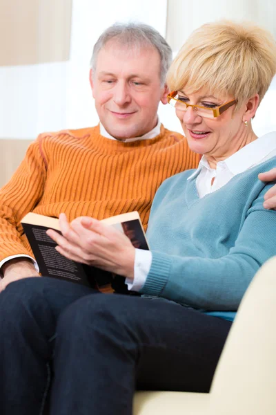 Idosos em casa lendo um livro juntos — Fotografia de Stock