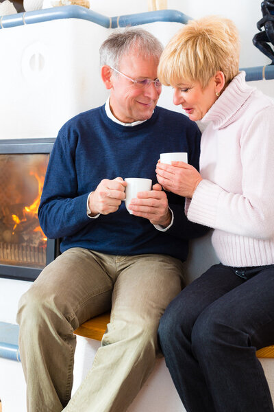 Seniors at home in front of fireplace with tea cup