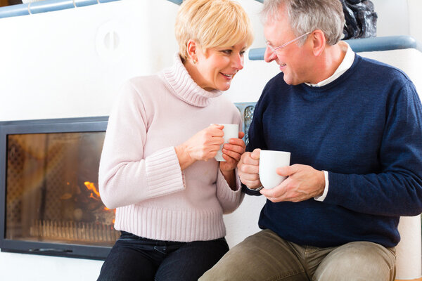 Seniors at home in front of fireplace with tea cup