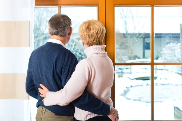 Senior couple looking or of the window hugging — Stock Photo, Image