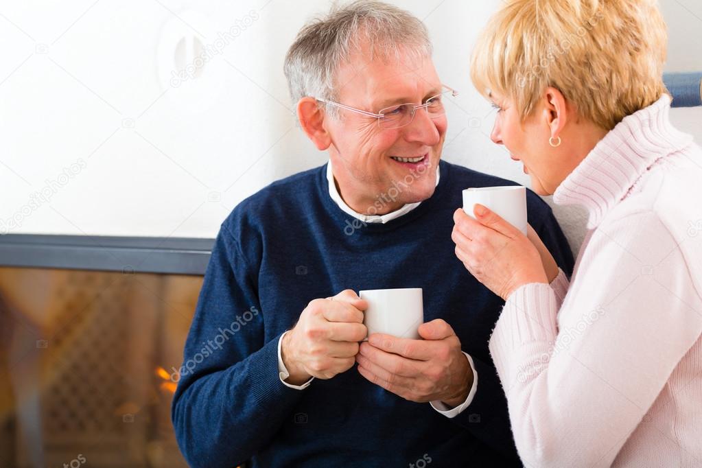 Seniors at home in front of fireplace with tea cup