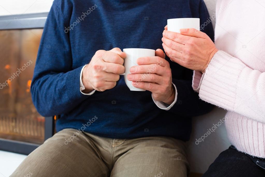 Seniors at home in front of fireplace with tea cup