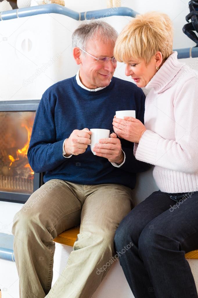 Seniors at home in front of fireplace with tea cup