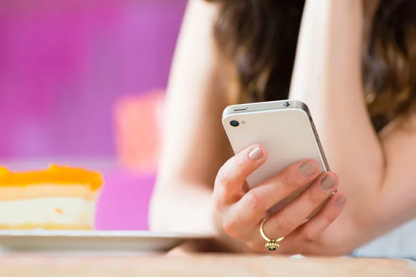 Young woman in ice cream parlor with phone texting — Stock Photo, Image