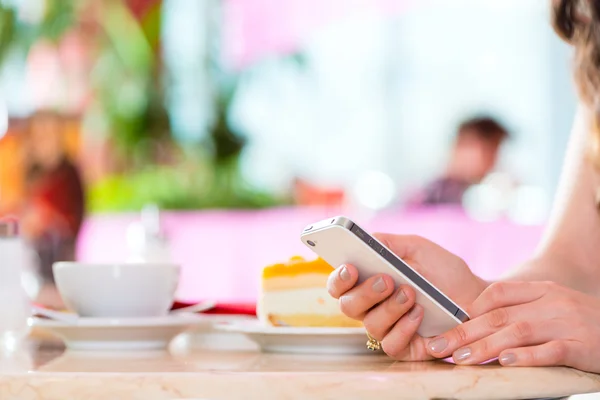 Молодая женщина в кафе с телефоном смс — стоковое фото