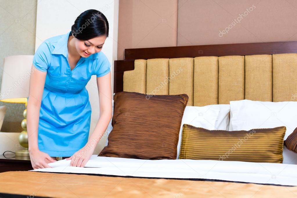 Chambermaid making bed in Asian hotel room