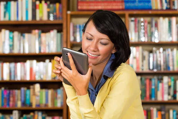 Menina na biblioteca lendo um e-book — Fotografia de Stock