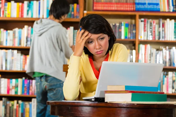 Chica joven en la biblioteca con el ordenador portátil —  Fotos de Stock