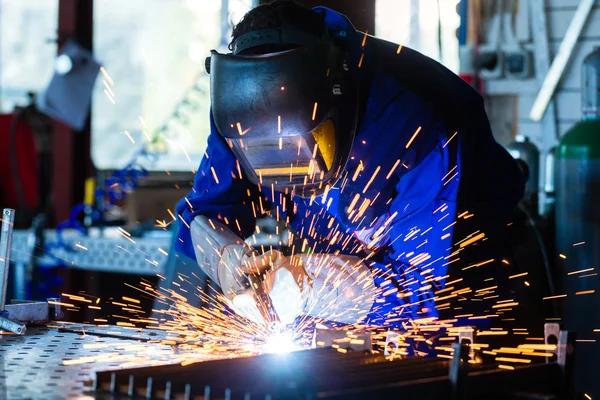 Svetsare svetsning metal i workshop med gnistor Stockfoto