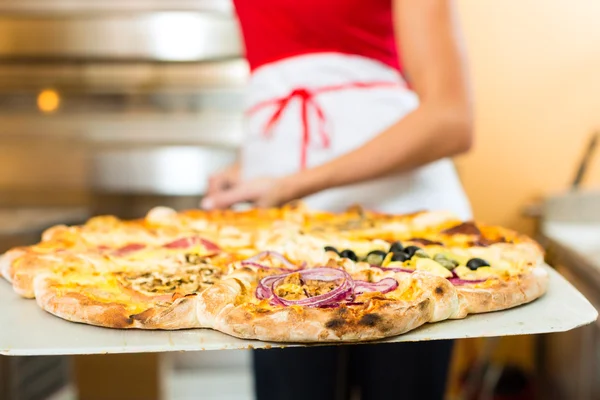 Mulher empurrando a pizza acabada do forno — Fotografia de Stock