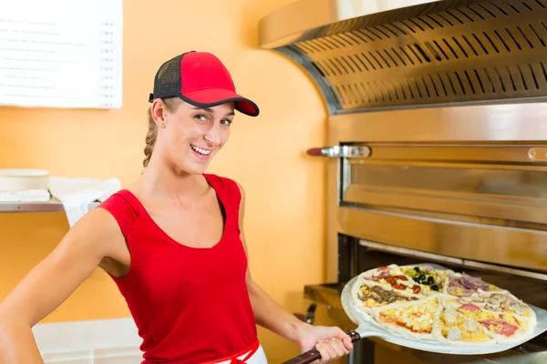 Vrouw duwen de pizza in de oven — Stockfoto