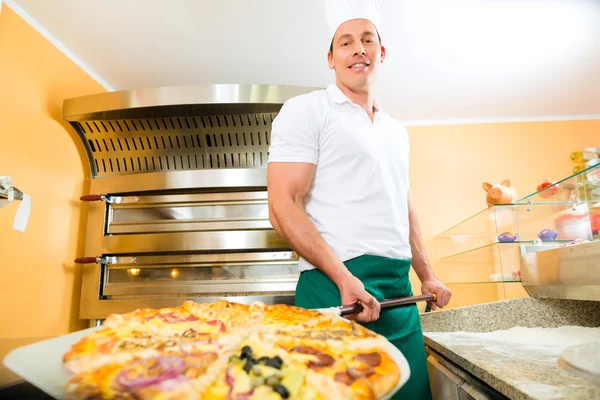 Mann schiebt die fertige Pizza aus dem Ofen — Stockfoto