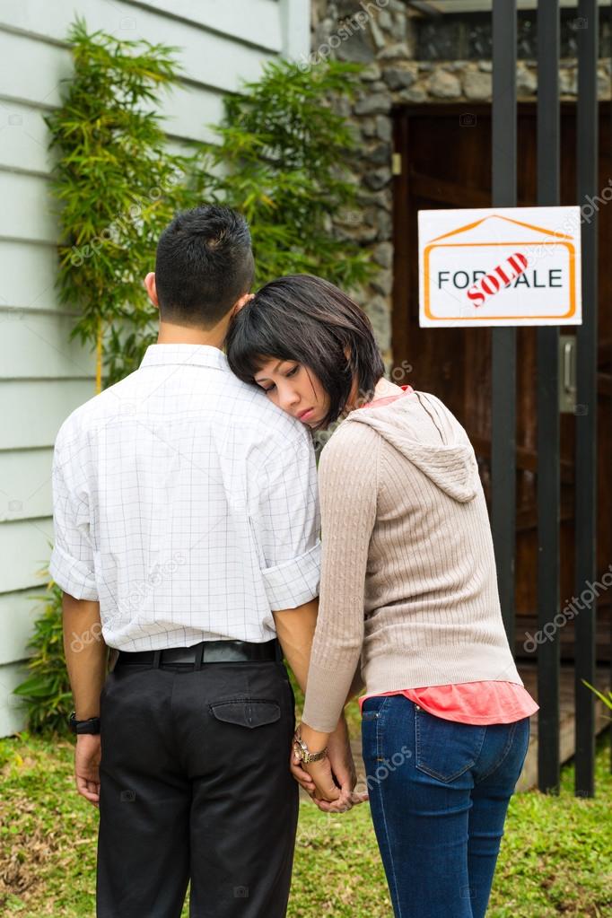 disappointed asian couple in front of a house