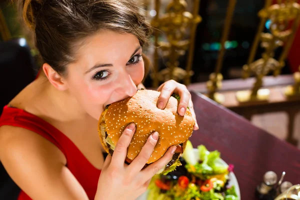 Woman in fine restaurant, she eats a burger — Stock fotografie