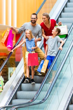 Aile alışveriş torbaları ile yürüyen merdiven üzerinde