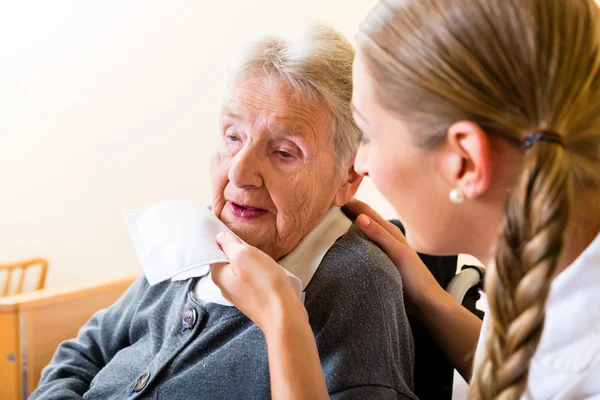 Nurse wiping mouth of senior woman in nursing home — Stock Photo, Image