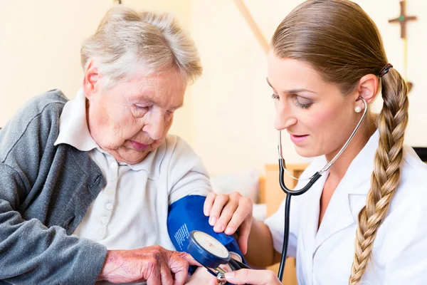 Nurse measuring blood pressure at senior patient — Stock Photo, Image