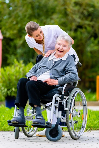 Nurse pushing senior woman in wheelchair on walk — Stock Photo, Image