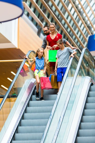 Famiglia in centro commerciale su scale mobili con borse — Foto Stock