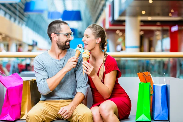 Casal comer sorvete em shopping center com sacos — Fotografia de Stock