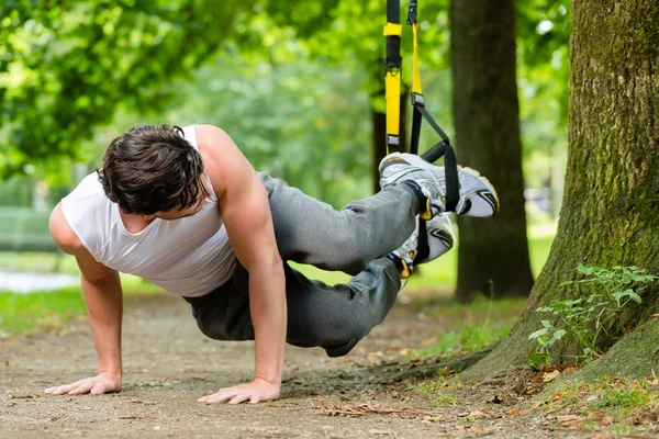 Hombre en el parque de la ciudad haciendo deporte entrenador de suspensión — Foto de Stock