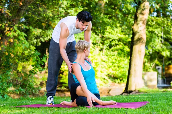 Mujer joven al aire libre haciendo yoga con entrenador —  Fotos de Stock