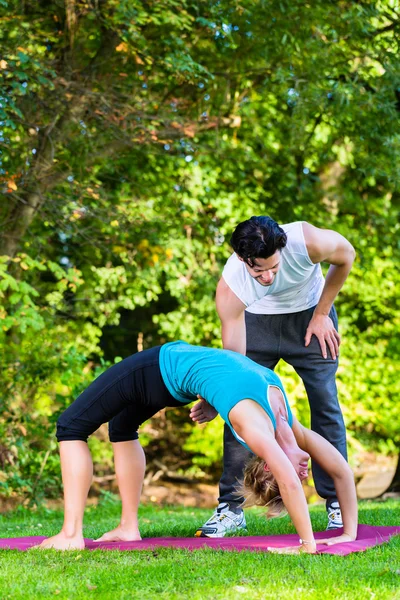 Giovane donna all'aperto facendo yoga con allenatore — Foto Stock