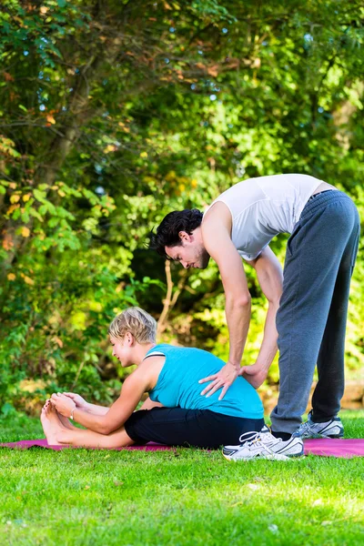 Young woman outdoors doing yoga with trainer — Stock Photo, Image