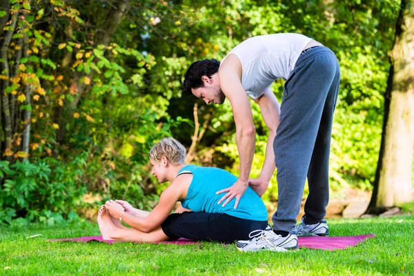 Young woman outdoors doing yoga with trainer — Stock Photo, Image