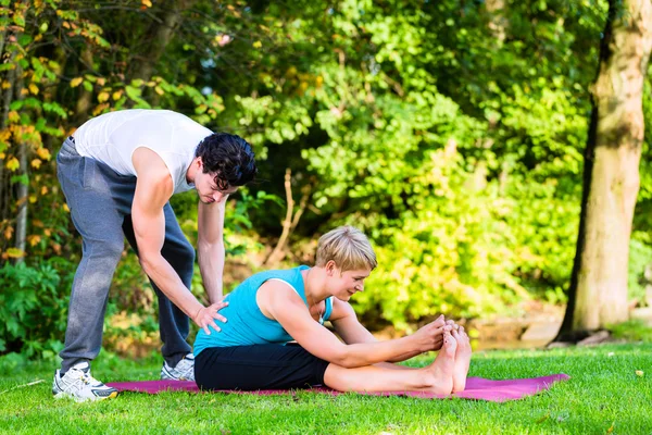 Young woman outdoors doing yoga with trainer — Stock Photo, Image