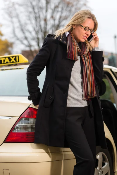 Young woman in front of taxi with phone — Stock Photo, Image