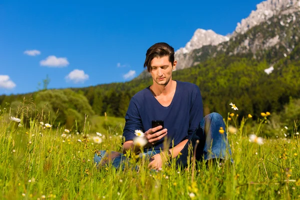 Людина з телефоном сидить у горах — стокове фото